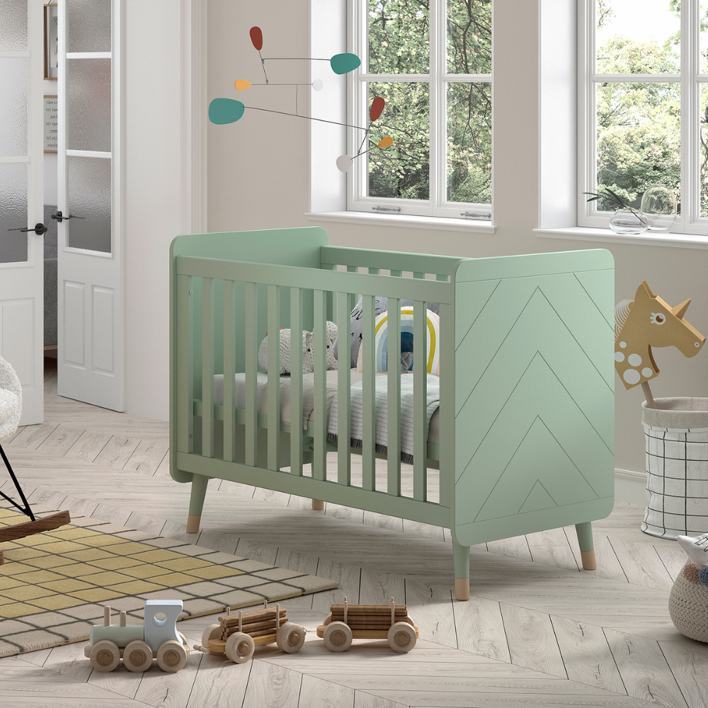 The Billy Baby Cot Bed in Olive Green features a geometric graphic design, golden accents and an adjustable slatted base, perfect for a modern nursery setup