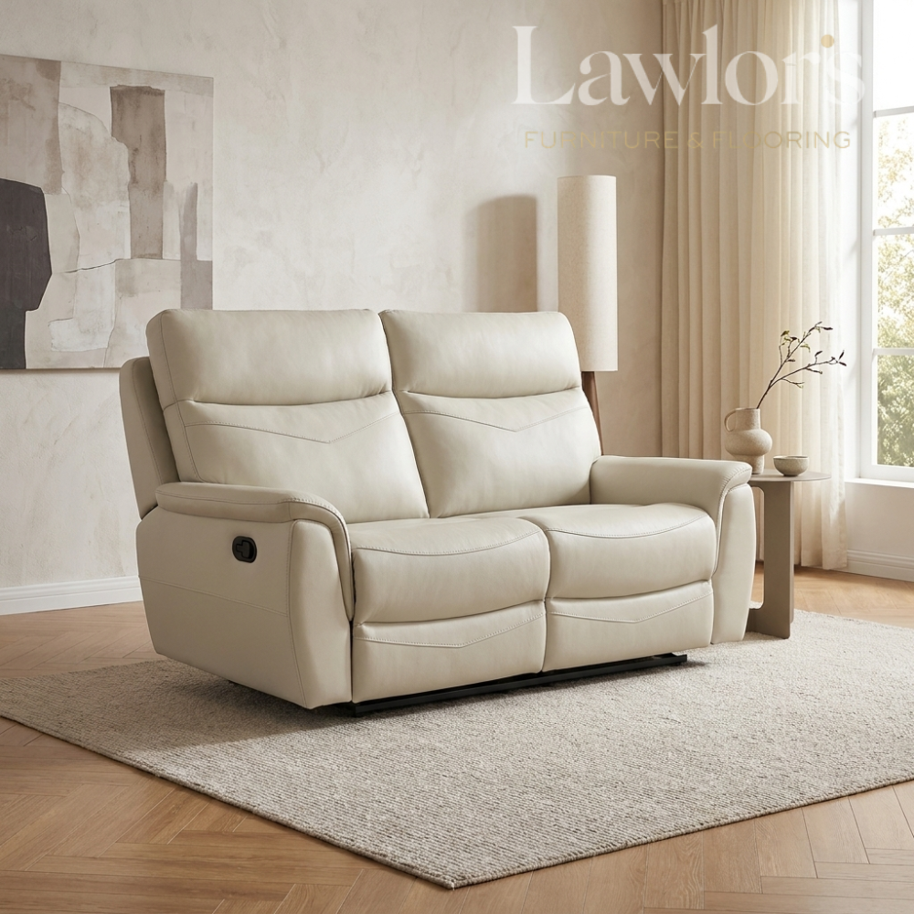 A cream-colored leather reclining loveseat sofa in a modern, sunlit living room setting with a textured rug, wooden floor, and side table.