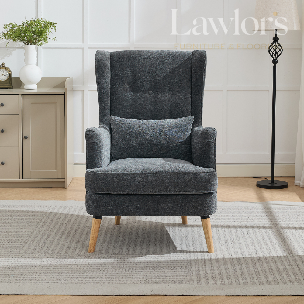 Grey armchair with a pillow on a rug in a room with a cabinet and lamp.