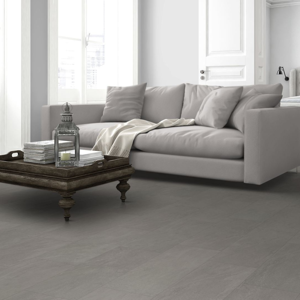 Light gray spc flooring in a bright, modern living room setting with a light gray sofa, a dark wooden coffee table, and a window in the background.