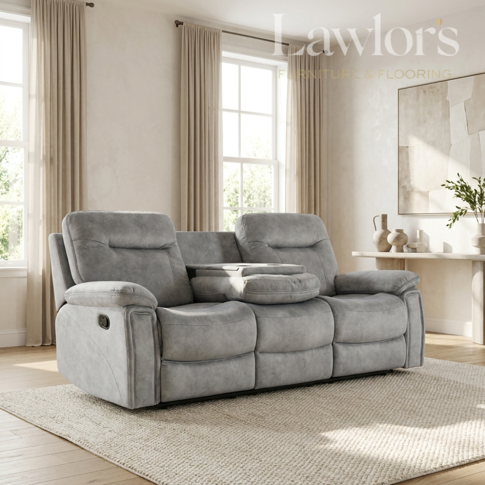 A gray reclining loveseat with two seat backs and a center console table, shown in a styled living room setting with beige curtains, a rug, and a console table.