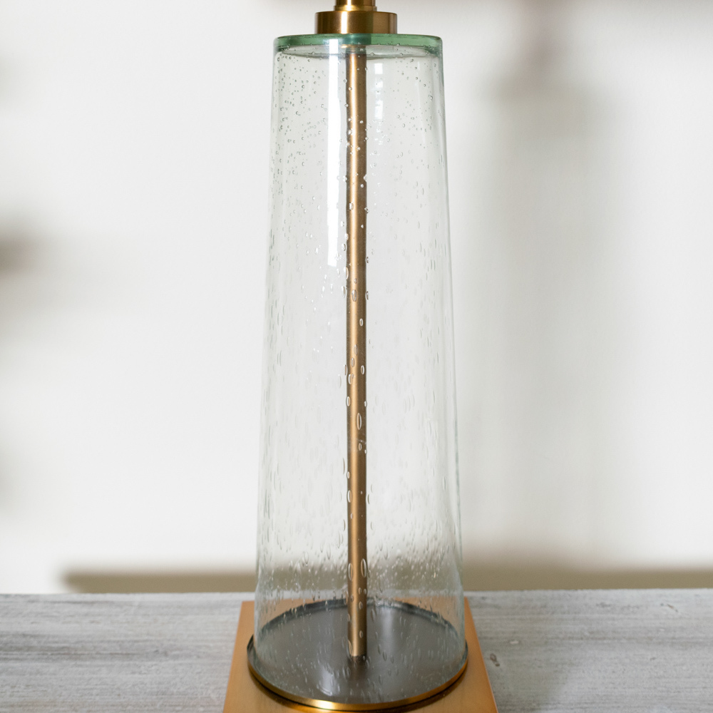 The elegant Amara Table Lamp Bubble Glass features a distinctive slanted base crafted from bubbled glass and brass fitting