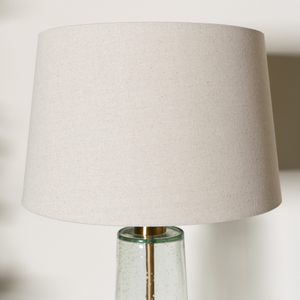 The elegant Amara Table Lamp Bubble Glass features a distinctive slanted base crafted from bubbled glass and brass fitting