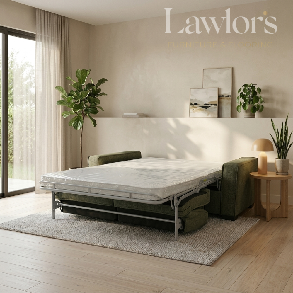 A Lawlor's brand sofa bed with a mattress on a metal frame, styled in a modern, sunlit bedroom with a green armchair, plants, and a side table.
