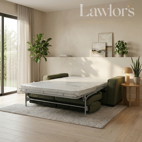 A Lawlor's brand sofa bed with a mattress on a metal frame, styled in a modern, sunlit bedroom with a green armchair, plants, and a side table.