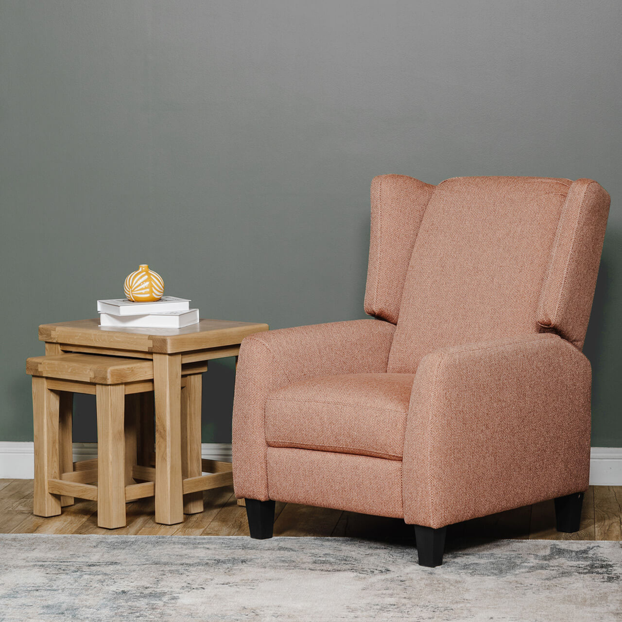 Brown armchair next to a wooden side table against a grey wall.