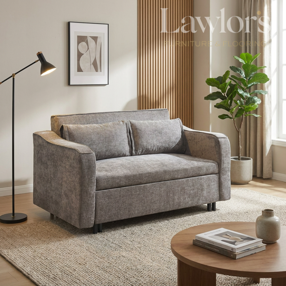 Grey sofa bed in a living room with a lamp, plant, and coffee table.