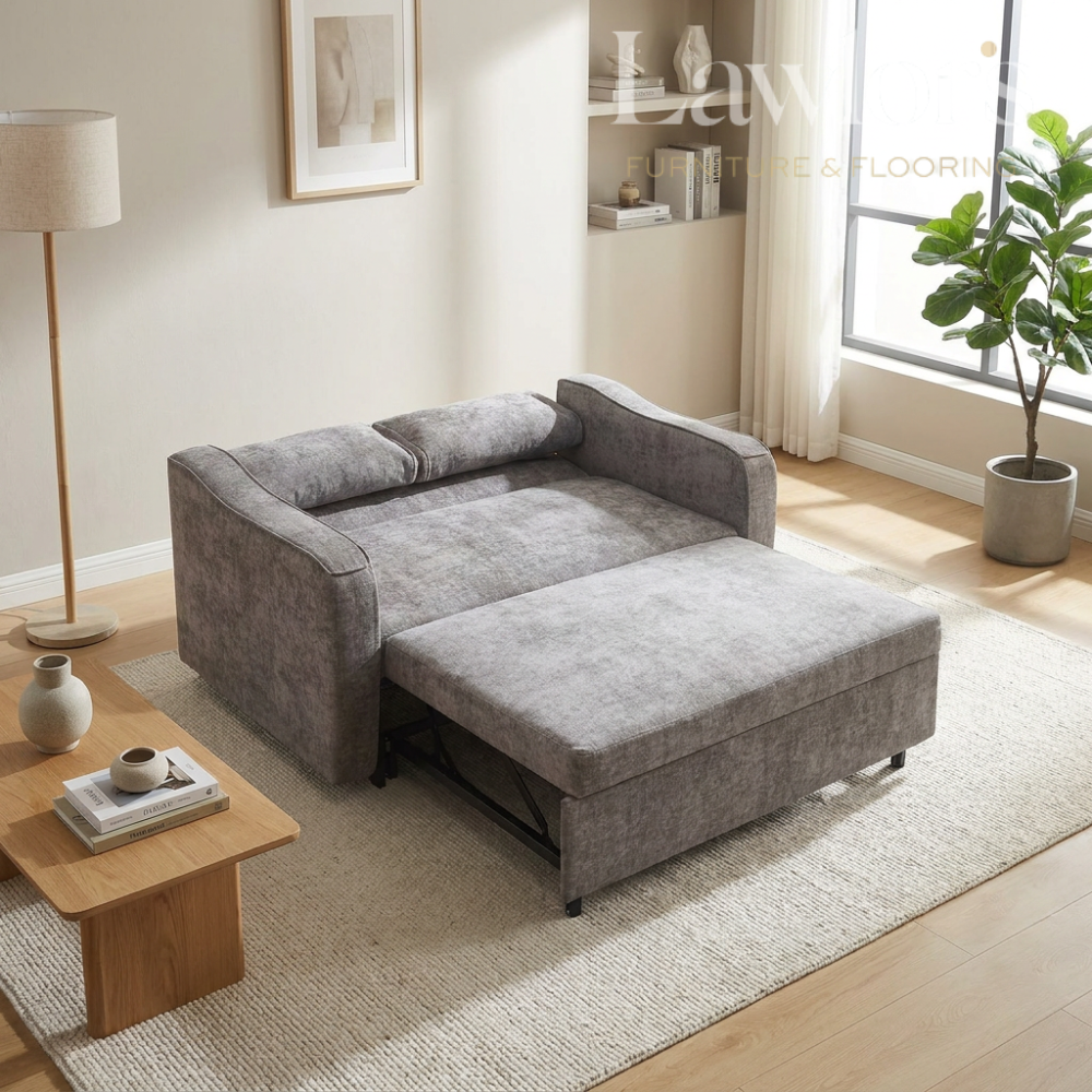Grey sectional opened sofa bed in a living room setting with a coffee table and decor items.