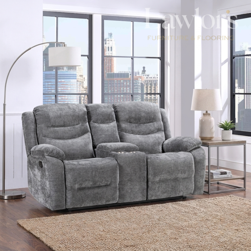 A gray plush 2 seater console reclining sofa shown in a modern living room setting with a floor lamp, side table, lamp, and city view windows.
