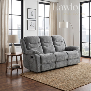 A gray reclining three seater sofa in a modern living room setting with wood floors, a woven rug, a side table with a lamp, and large windows.