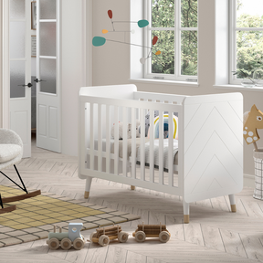 The Billy Baby Cot Bed in Satin White features a geometric graphic design, golden accents and an adjustable slatted base, perfect for a modern nursery setup