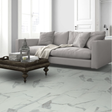 A modern living room scene featuring a light gray fabric sofa, a dark wood coffee table with books and a lantern, and a large white marble floor with gray veining.