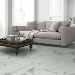 A modern living room scene featuring a light gray fabric sofa, a dark wood coffee table with books and a lantern, and a large white marble floor with gray veining.