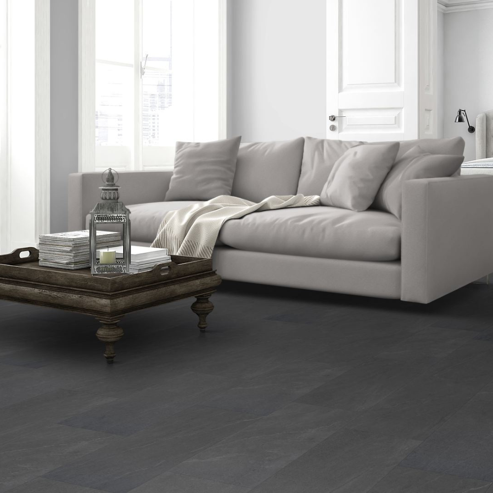 Dark charcoal gray spc flooring shown in a bright, modern living room setting with a light gray sofa and a rustic wooden coffee table.