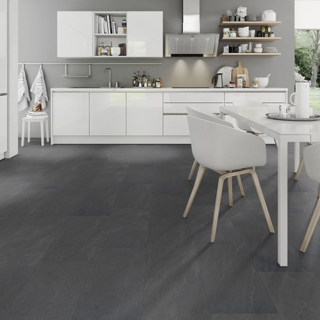 Dark charcoal gray stone-look floor tiles in a modern white kitchen setting, shown from a high angle with white dining chairs and a white table in the foreground.