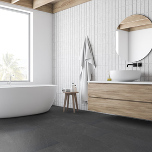 A modern bathroom interior with a freestanding white bathtub by a large window, white wall tiles, a light wood floating vanity with a white vessel sink and black faucet, a round wood-framed mirror, a small wooden stool, and a draped white towel.