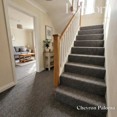 Staircase with gray herringbone patterned carpet, leading to a living room.