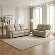 A beige leather reclining loveseat and matching armchair arranged on a large textured area rug in a bright, modern living room with wood floors, paneled walls, and tall windows.