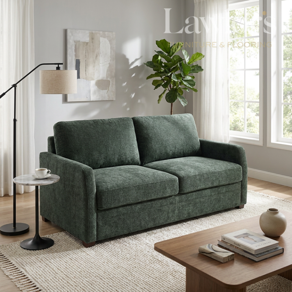 Green sofa bed in a living room with a coffee table, lamp, and plant.