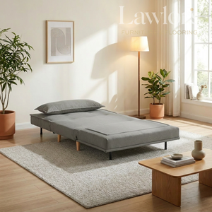 Grey sofa bed in a living room setting with plants and a lamp.