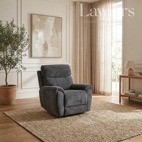 A dark gray upholstered recliner chair placed on a woven area rug in a bright, modern living room with wood floors, beige curtains, a potted tree, and wall art.
