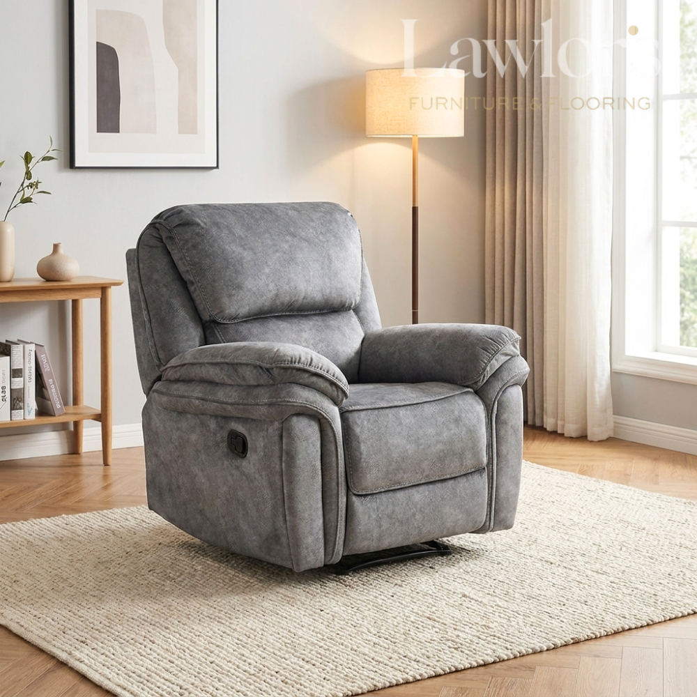 A dark grey upholstered recliner chair placed in a bright living room with a floor lamp, window, curtains, side table, and rug.