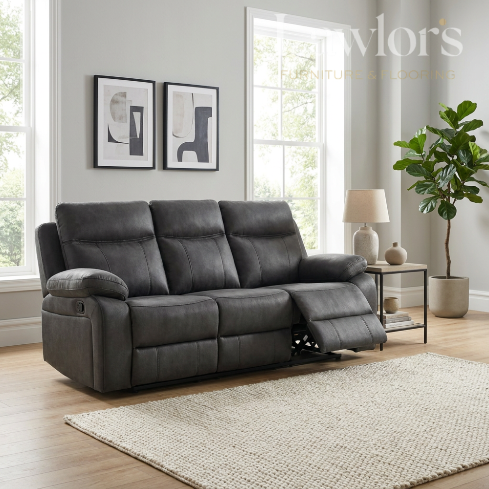 Gunmetal grey 3 seater reclining sofa in a living room with a lamp, plant, and framed pictures on the wall.