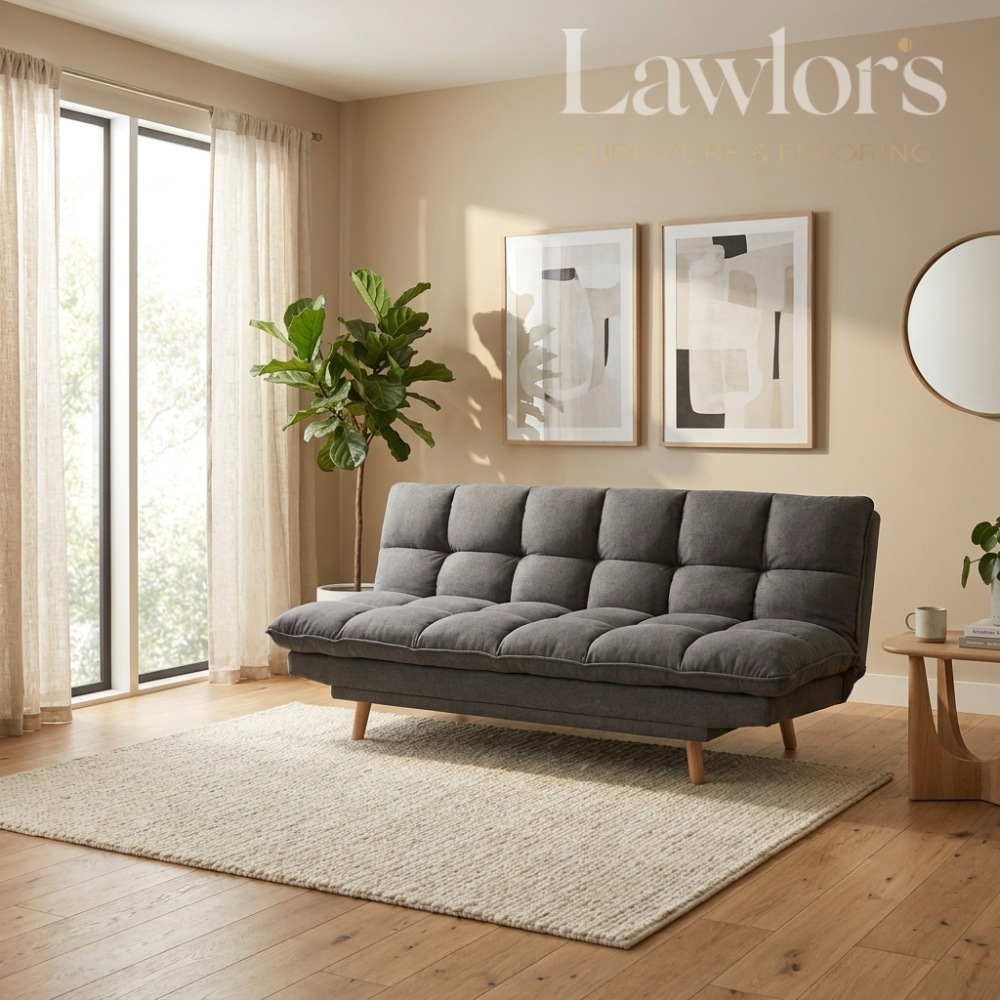 A modern gray tufted fabric sofa bed with wooden legs, styled in a warm beige living room on a cream rug