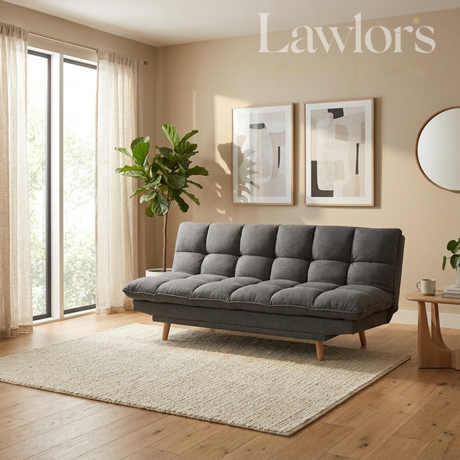A modern gray tufted fabric sofa bed with wooden legs, styled in a warm beige living room on a cream rug