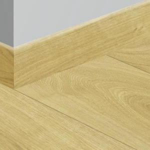 Light oak wood flooring planks with a natural wood grain finish, shown meeting a white baseboard against a light gray wall.