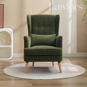 Green armchair with a pillow on a wooden floor in a room with a beige wall and a white shelf.
