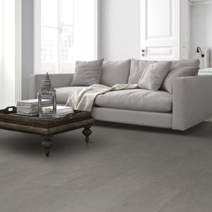 Light gray spc flooring in a bright, modern living room setting with a light gray sofa, a dark wooden coffee table, and a window in the background.