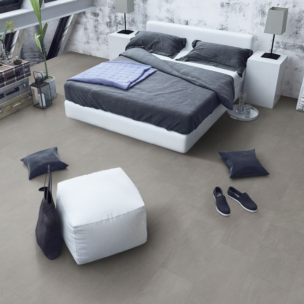 A modern bedroom scene showing a white platform bed with dark gray bedding, flanked by white bedside tables and lamps, with a white ottoman and dark throw pillows on a light gray spc floor.