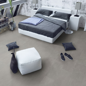 A modern bedroom scene showing a white platform bed with dark gray bedding, flanked by white bedside tables and lamps, with a white ottoman and dark throw pillows on a light gray spc floor.
