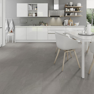 A modern kitchen interior with white cabinets, a white dining table, white chairs with light wood legs, and large gray floor tiles. The image appears to emphasize the spc flooring, with the floor occupying most of the frame and the kitchen serving as contextual staging.