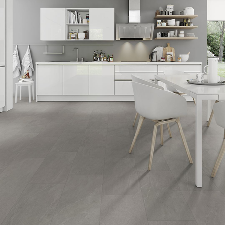 A modern kitchen interior with white cabinets, a white dining table, white chairs with light wood legs, and large gray floor tiles. The image appears to emphasize the spc flooring, with the floor occupying most of the frame and the kitchen serving as contextual staging.