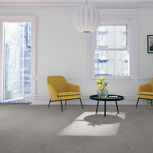 A modern living room interior with light gray spc flooring, two yellow armchairs, a black round coffee table with a vase of yellow flowers, a white paper lantern pendant light, and white walls with window trim.