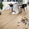 Light oak wood plank flooring shown in a modern dining room setting with a table, chairs, and scattered toy blocks on the floor.
