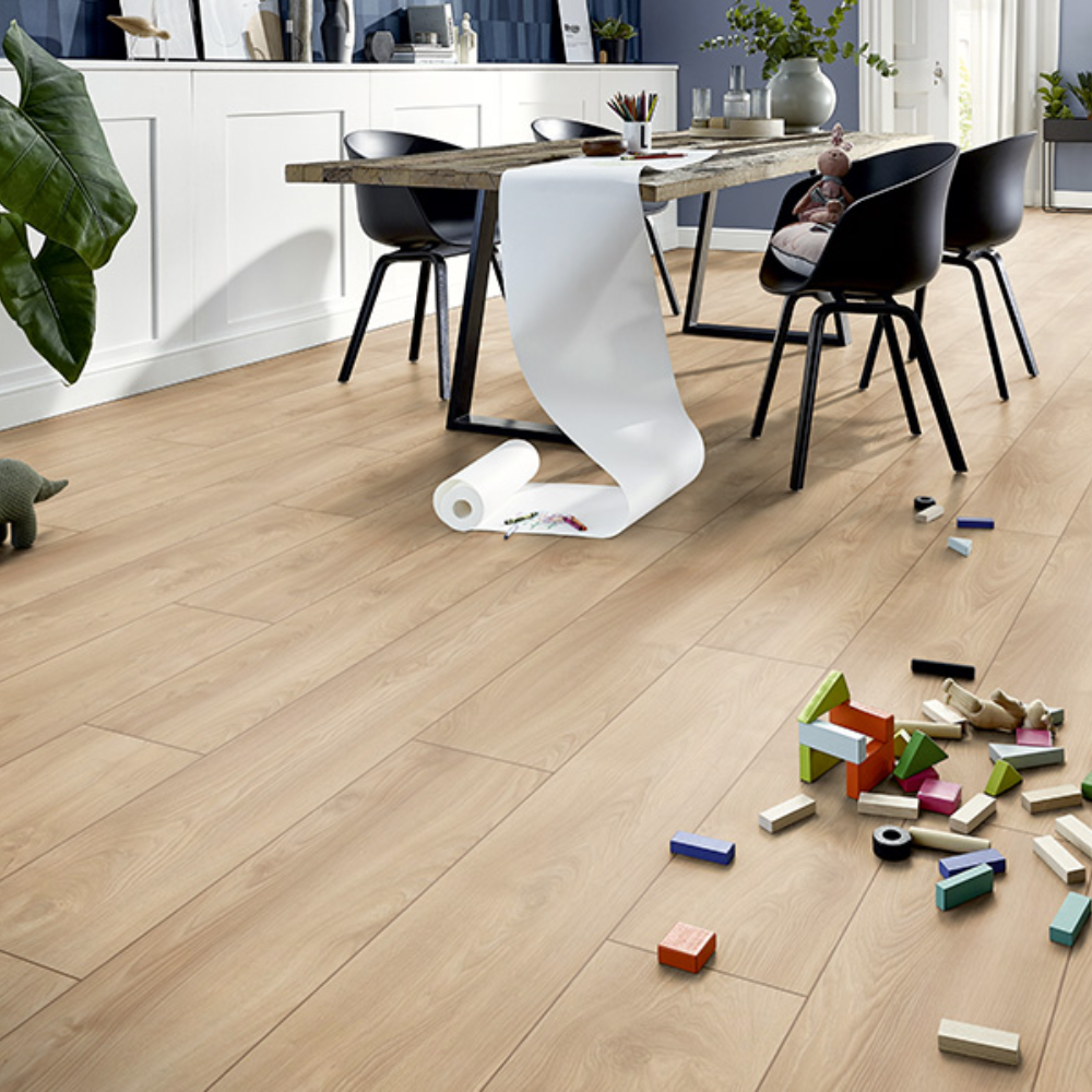 Light oak wood plank flooring shown in a modern dining room setting with a table, chairs, and scattered toy blocks on the floor.