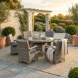 Outdoor garden furniture patio set with table and chairs on a stone patio with plants and a pergola in the background.