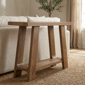 Wooden console table in a living room setting with a sofa and plant in the background.