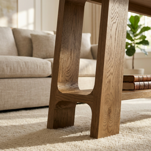 Wooden console table in a living room setting with a sofa and plant in the background