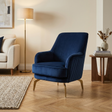 Blue armchair in a living room setting with a lamp and table in the background.
