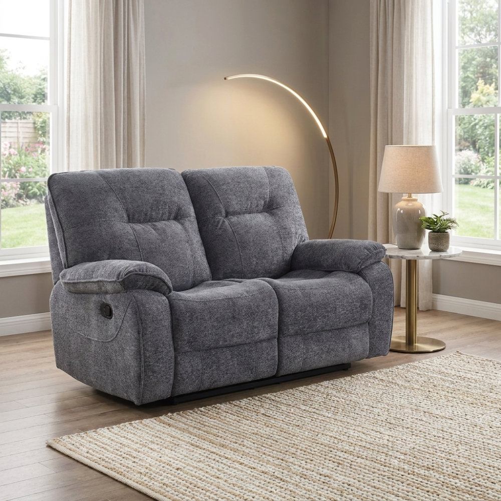 Dark grey 2 seater recliner sofa in a living room with a lamp and window view.