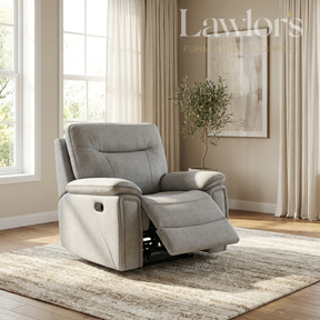 A light gray fabric recliner chair with the footrest extended, placed on a textured beige rug in a bright living room. The room has beige walls, curtains, a window, and a potted tree.