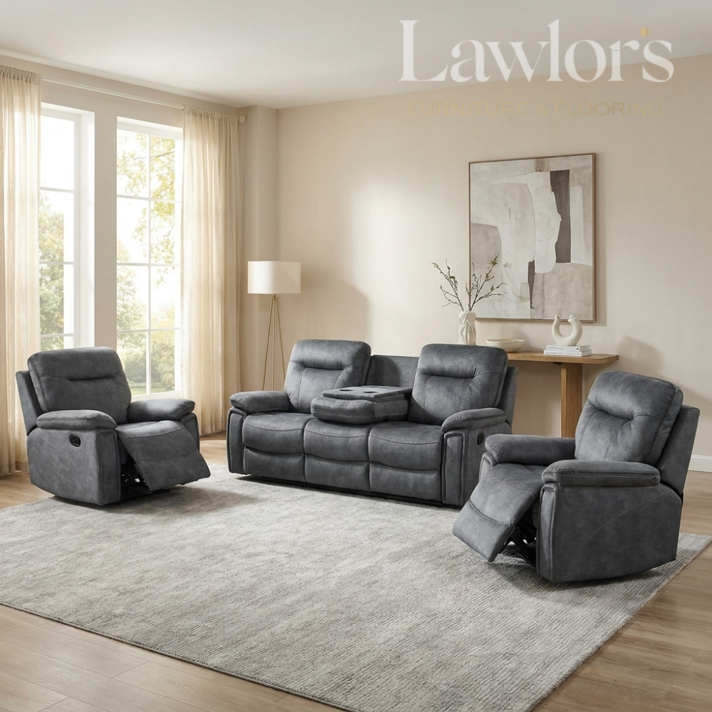 A staged living room showing a dark gray upholstered recliner, a matching three-seat sofa, and a third recliner on a large light gray rug. The room has beige walls, wood flooring, a floor lamp, and a wall art piece.