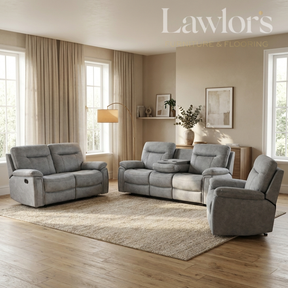 A staged living room showing a coordinated gray upholstered furniture set: a loveseat, a reclining sofa, and a matching armchair arranged on a large beige rug over hardwood flooring. The room has beige walls, tall windows with beige curtains, a floor lamp, and wall art.
