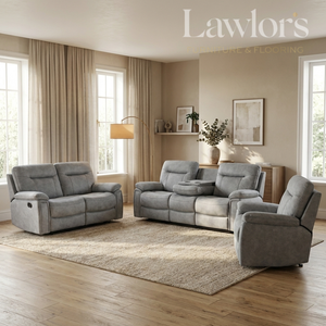 A staged living room showing a coordinated gray upholstered furniture set: a loveseat, a reclining sofa, and a matching armchair arranged on a large beige rug over hardwood flooring. The room has beige walls, tall windows with beige curtains, a floor lamp, and wall art.