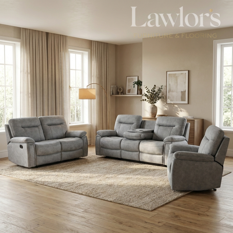 A staged living room showing a coordinated gray upholstered furniture set: a loveseat, a reclining sofa, and a matching armchair arranged on a large beige rug over hardwood flooring. The room has beige walls, tall windows with beige curtains, a floor lamp, and wall art.