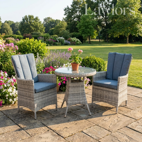 Outdoor garden furniture patio set with two chairs and a table on a stone patio, surrounded by flowers and greenery.